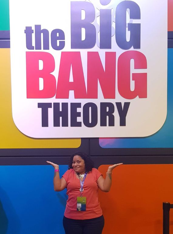 flavia-neves-2 Imagem de Flávia Neves ma frente de um banner da série The Big Bang Theory